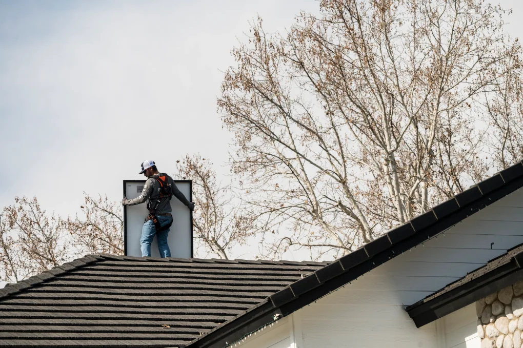 Solar panel installer holding a solar panel on top of a roof