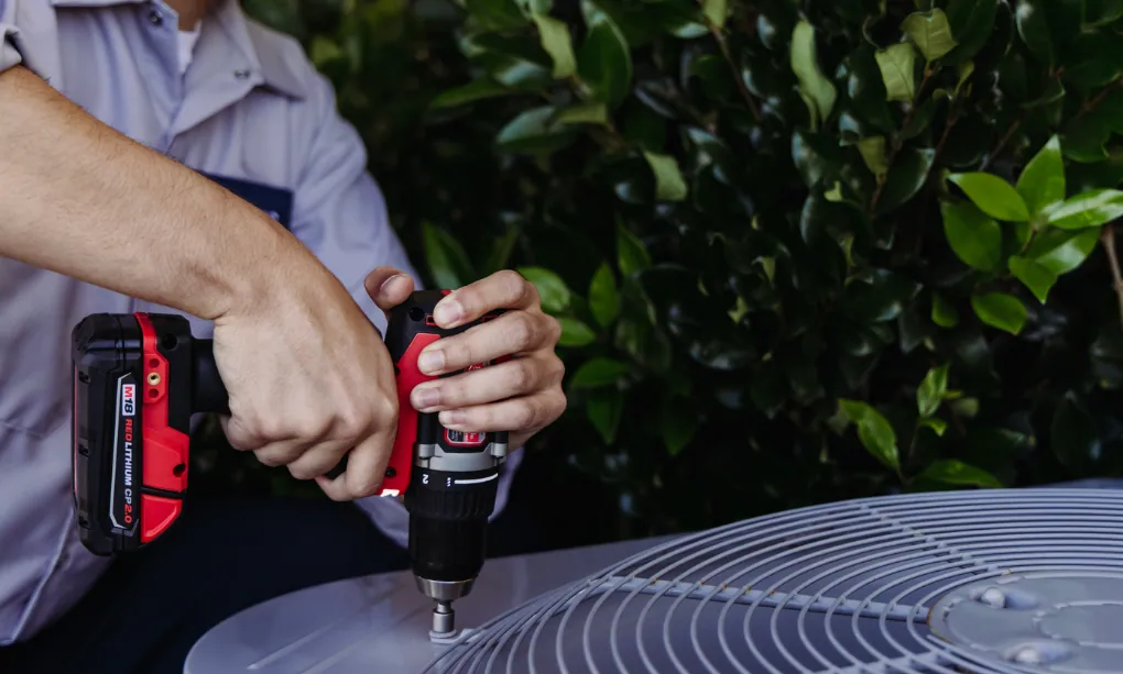 HVAC professional with a drill repairing a condenser unit
