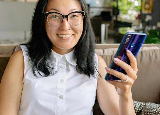 Smiling woman sitting on a couch holding a smartphone.