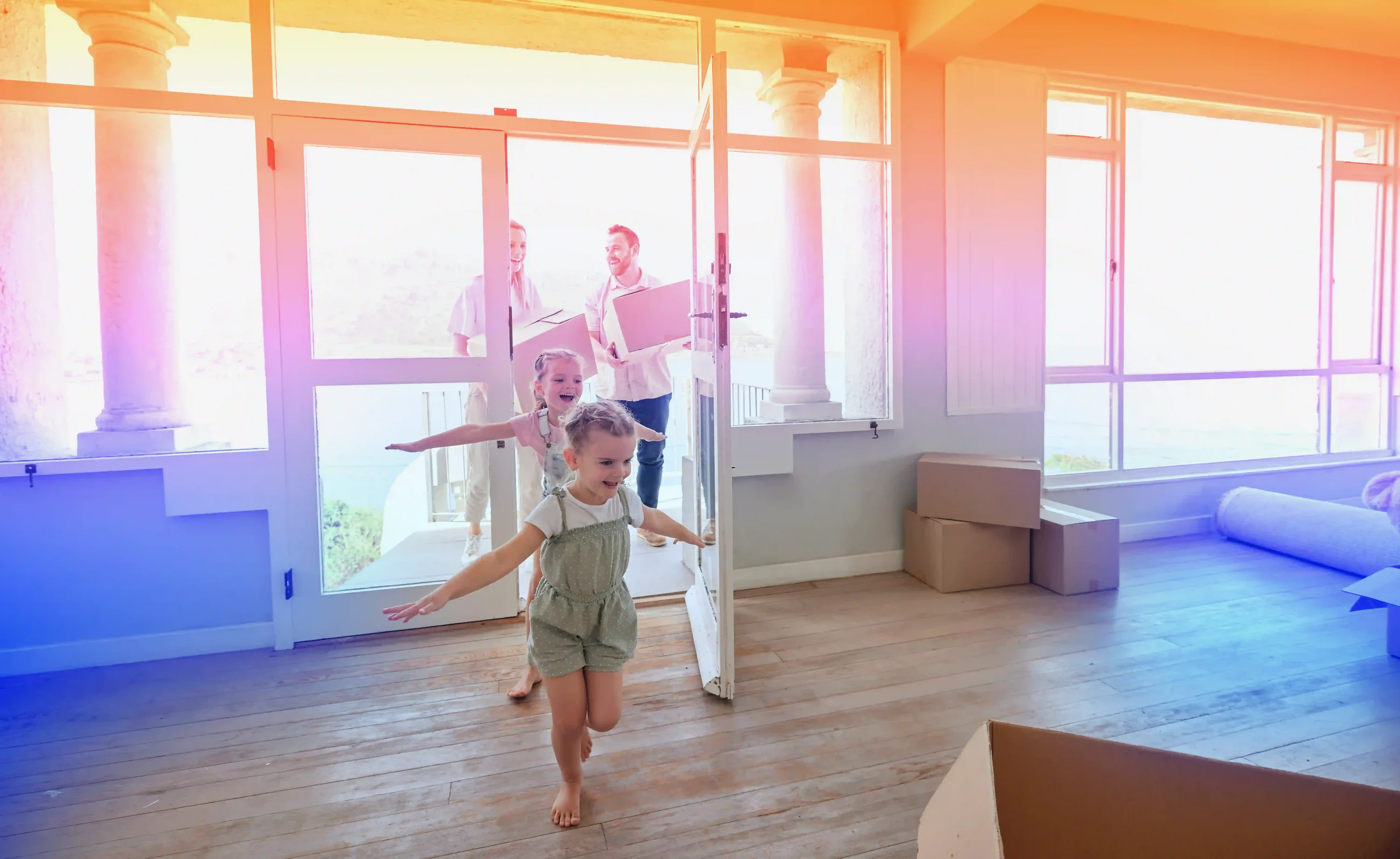 Two young children excitedly running into a new home as their parents follow behind carrying moving boxes, with unpacked boxes scattered around the room.